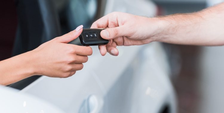 cropped-shot-of-man-giving-car-key-to-woman-at-dea-8BYW2C2